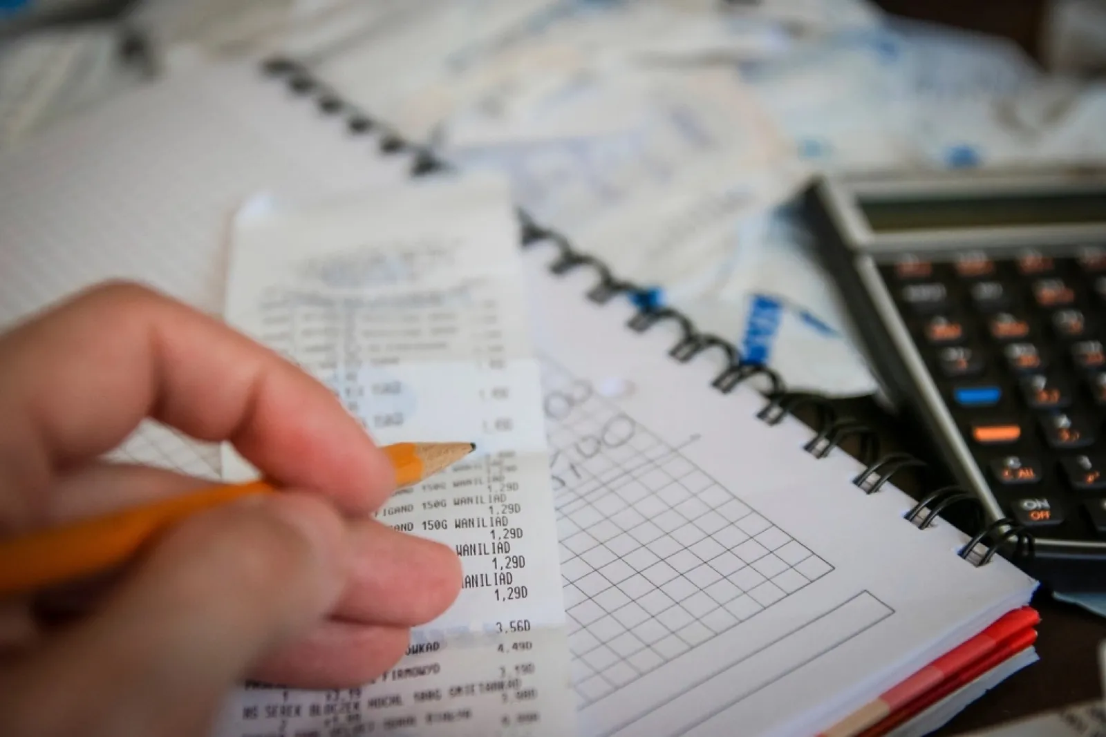 Hand holding a pencil over a paper receipt beside a notebook and calculator