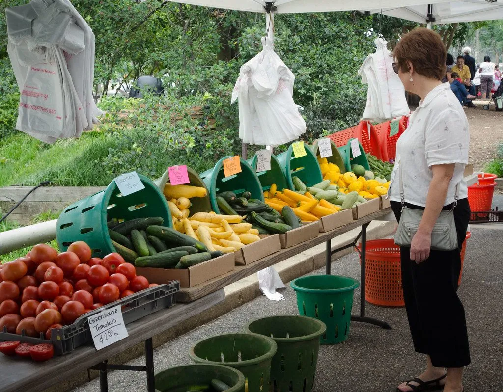 A shopper at a farmers market stand with tomatoes, squash, and cucumbers