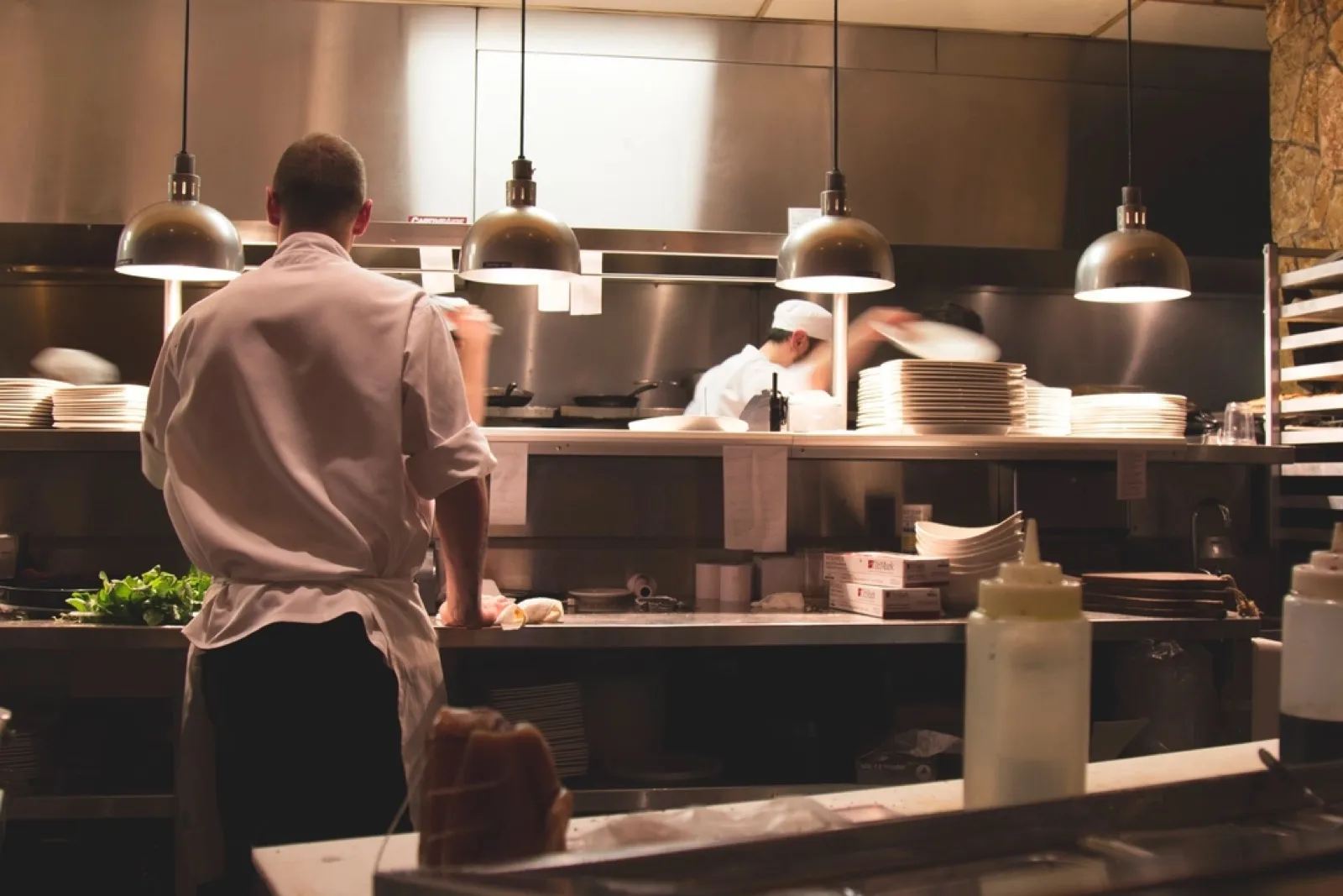 Chef in a white jacket working at the pass of a commercial kitchen under heat lamps